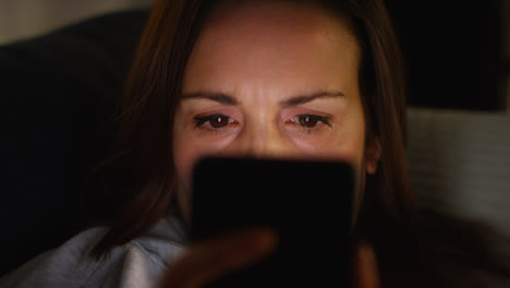 Close-Up-Of-Anxious-Woman-Sitting-On-Sofa-At-Home-At-Night-Looking-At-Mobile-Phone-Concerned-About-Social-Media-Or-Bad-News-1